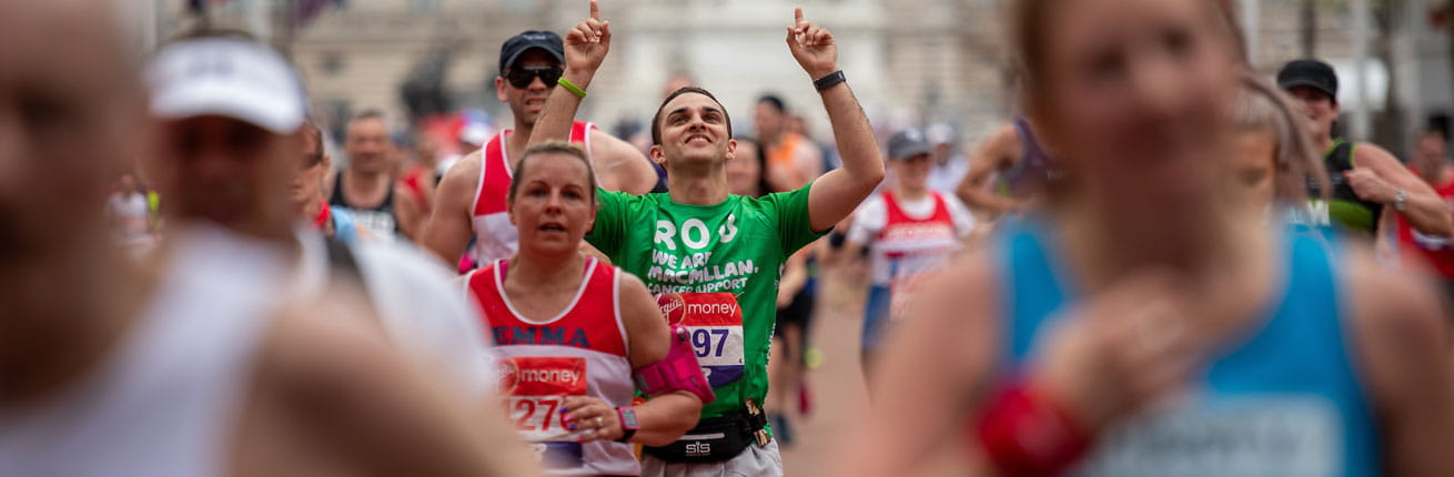A macmillan charity runner points to the sky as he nears the finish line
