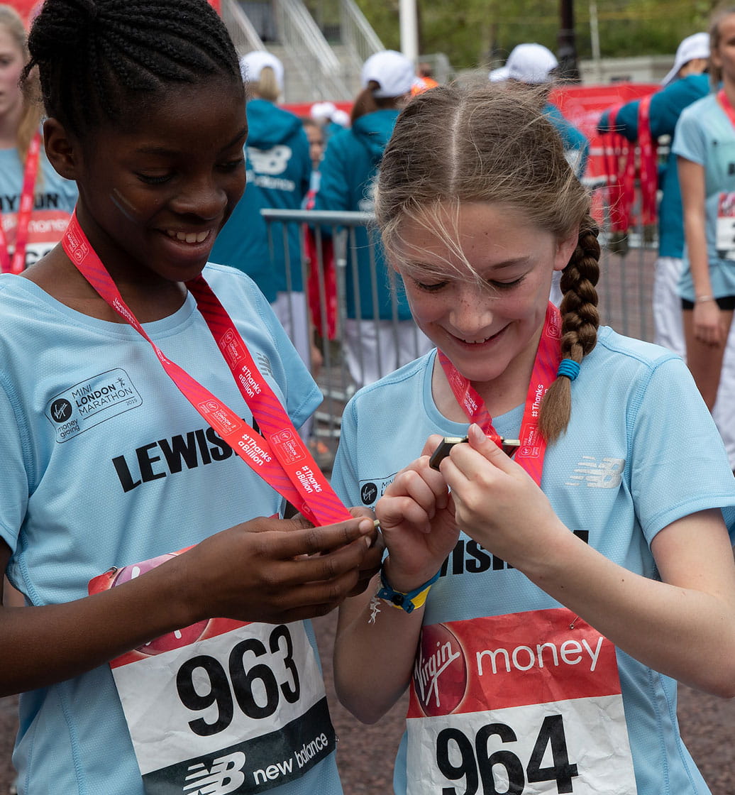 Two runners admire their medals at the Virgin Money Giving Mini London Marathon