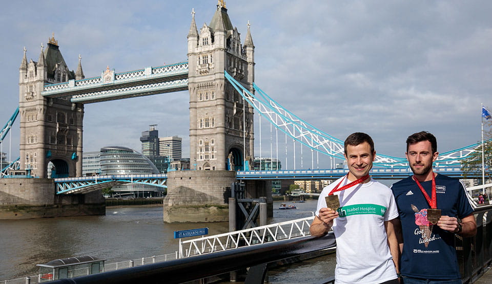 David Wyeth and Matthew Rees in front of Tower Bridge with their Virgin Money London Marathon medals