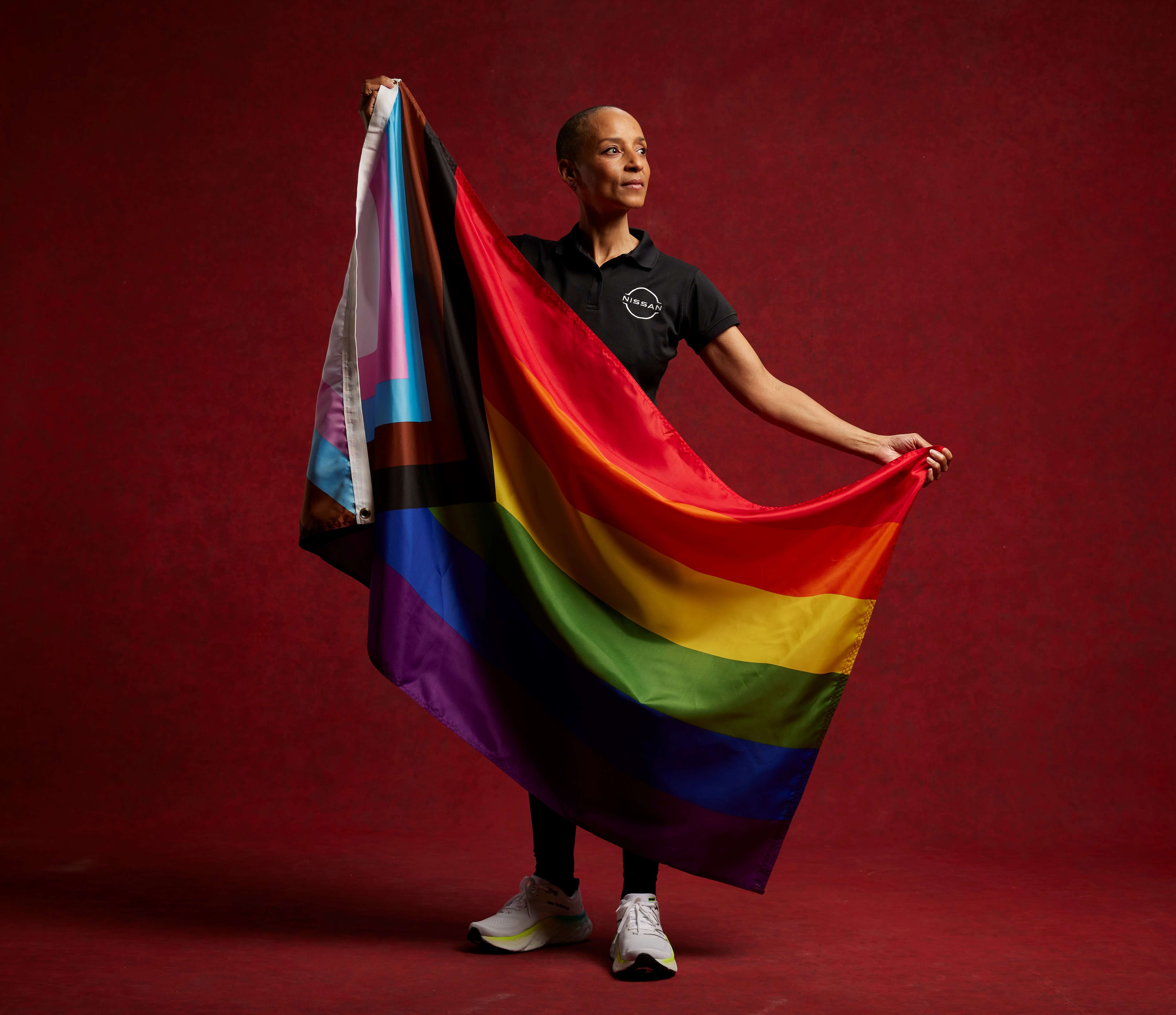 Adele Roberts stands holding a rainbow flag