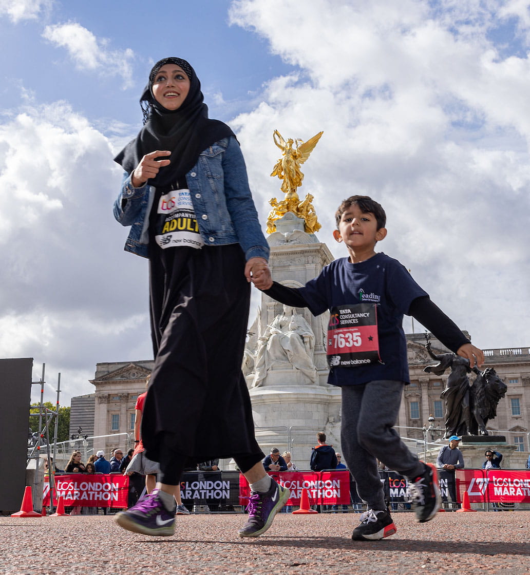 Mom and son running and holding hands and Buckingham Palace in the background in the TCS Mini London Marathon 2022