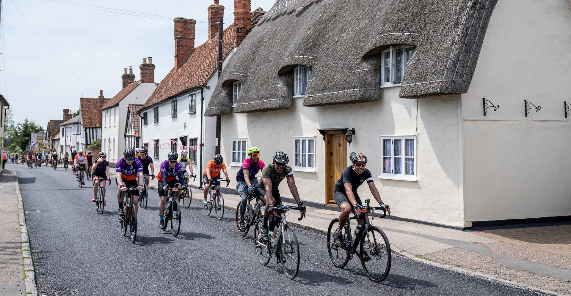 Cyclists ride past a thatched cottage