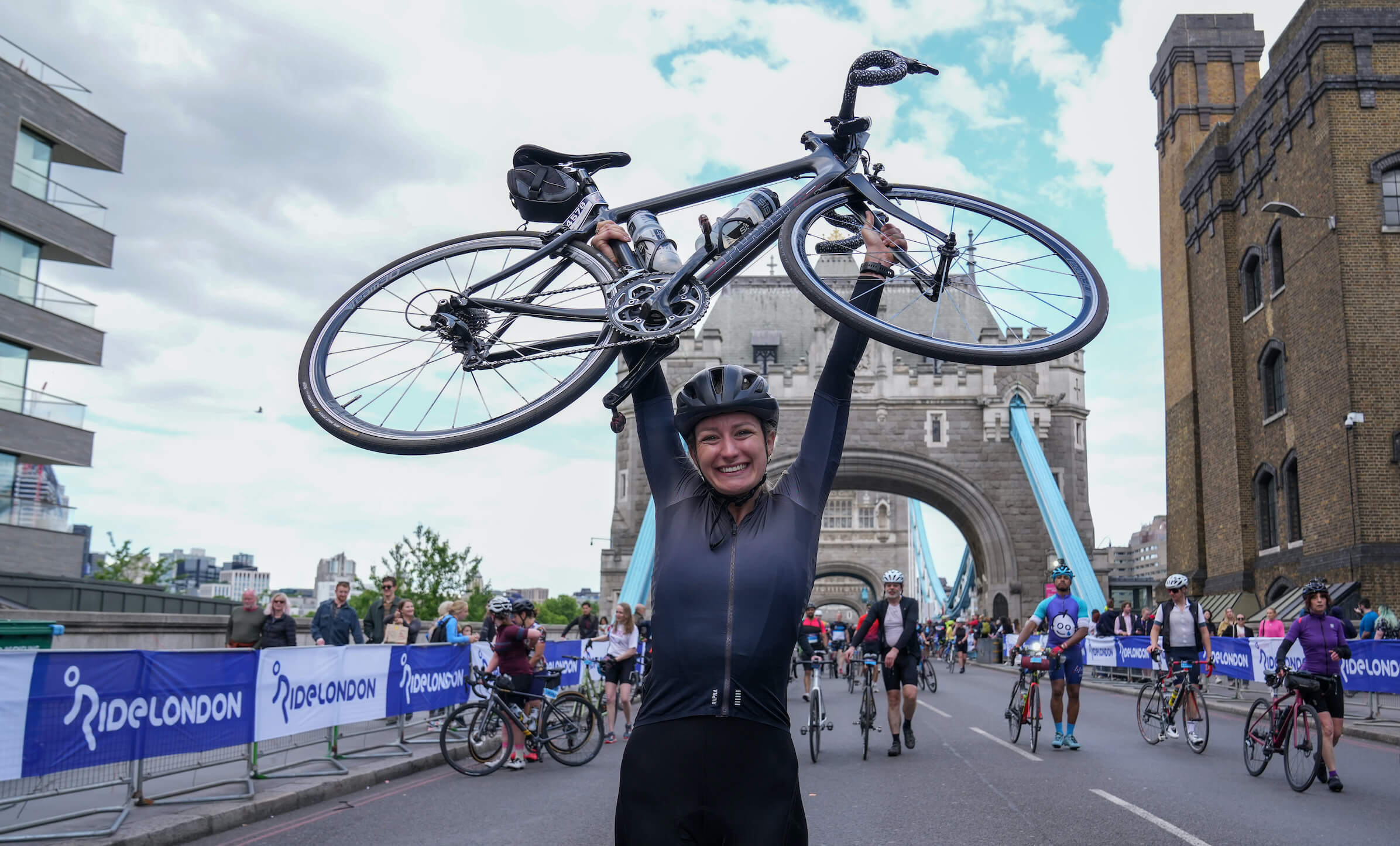 A happy cyclist lifts her bike above her head at Tower Bridge