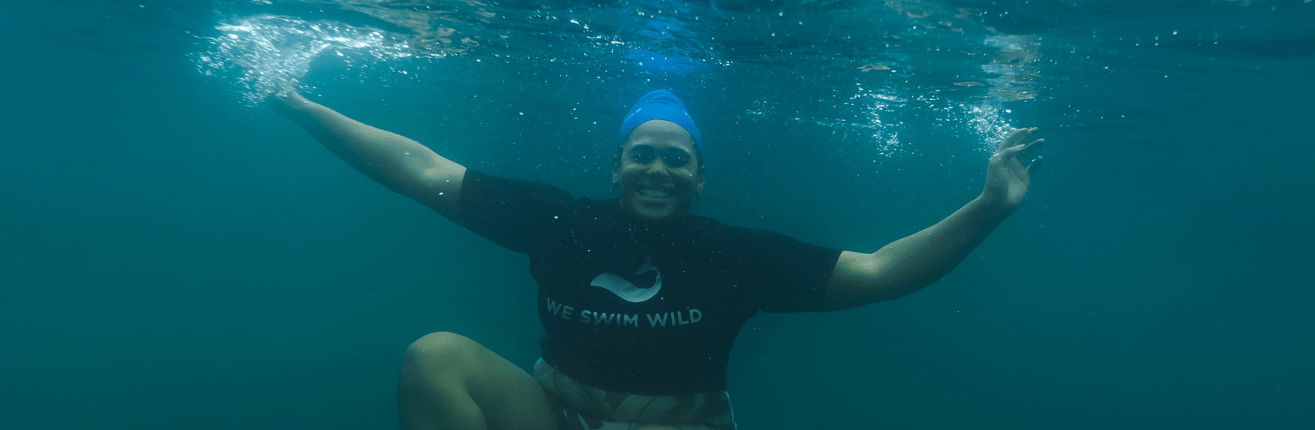 A photo of Shareefa in swimming cap and kit, smiling underwater 
