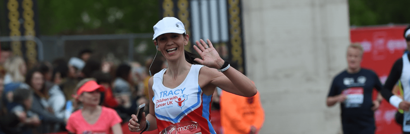 Photo of Tracy running the London Marathon, waving at the camera wearing a Children with Cancer charity top