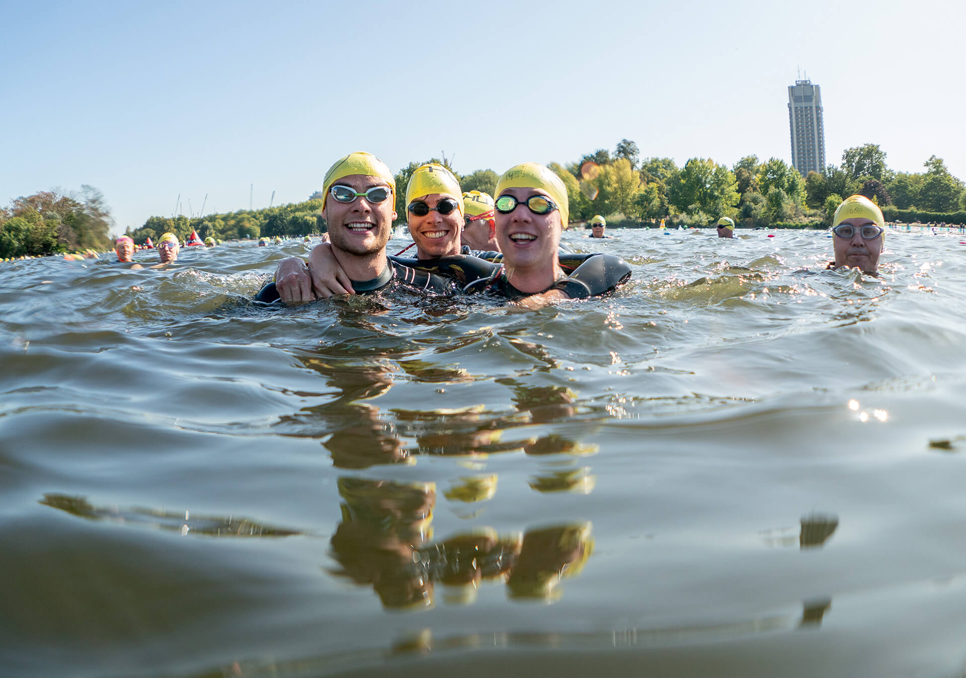 Three swimmers smiling together in the Serpentine lake