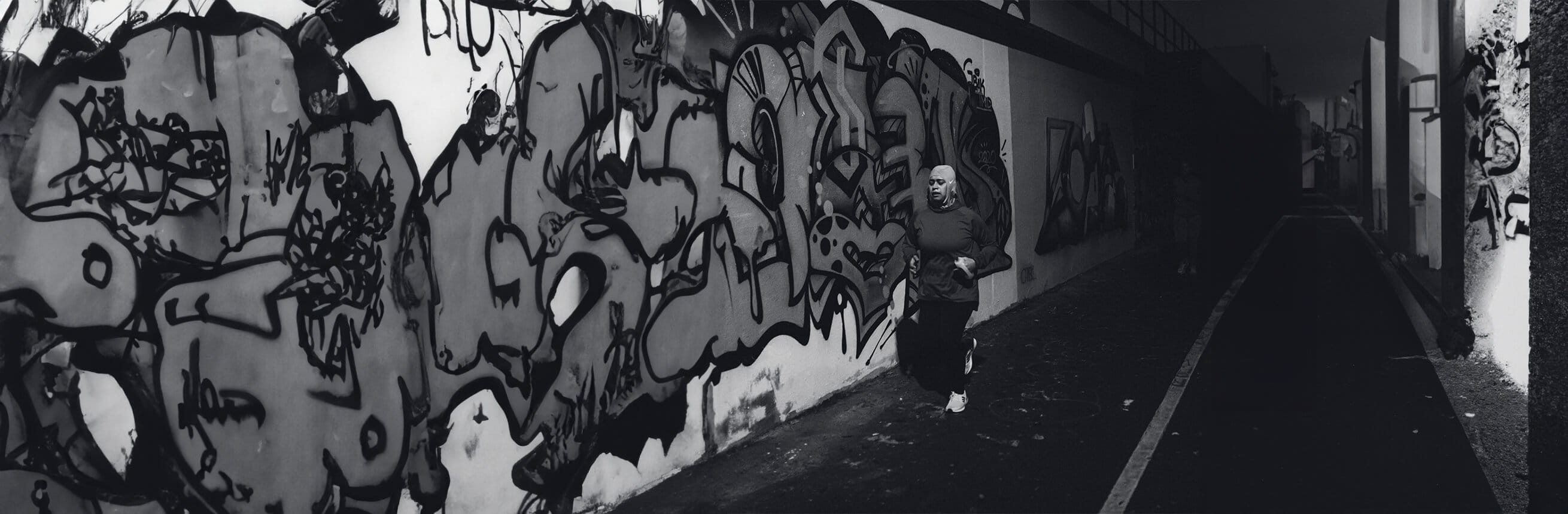 Local runner, Ruba Talukdar running. through an urban alley with graffiti on the walls